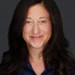 A woman with long, dark hair and a slight smile is wearing a navy blue shirt. The background is a solid dark color, reminiscent of the tranquil settings often utilized in Fertility Treatments Long Island.