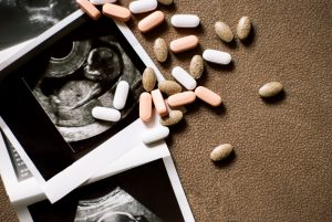 Scattered pink, white, and beige pills lie on a textured brown surface next to three black-and-white ultrasound images of a developing fetus, suggesting the intricate journey of fertility treatments in Long Island.