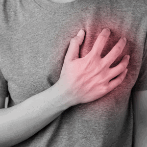 A person wearing a grey t-shirt clutches their chest with their right hand, and the area around the hand is highlighted in red, suggesting pain or discomfort in the chest. This scene underscores the importance of Pain Management Long Island for relief.