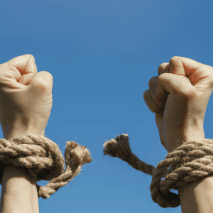 Two hands, with rope loosely wrapped around the wrists, are raised in the air against a clear blue sky. The image conveys a sense of liberation or breaking free from restraints, much like how Pain Management Long Island offers relief and freedom from chronic discomfort.